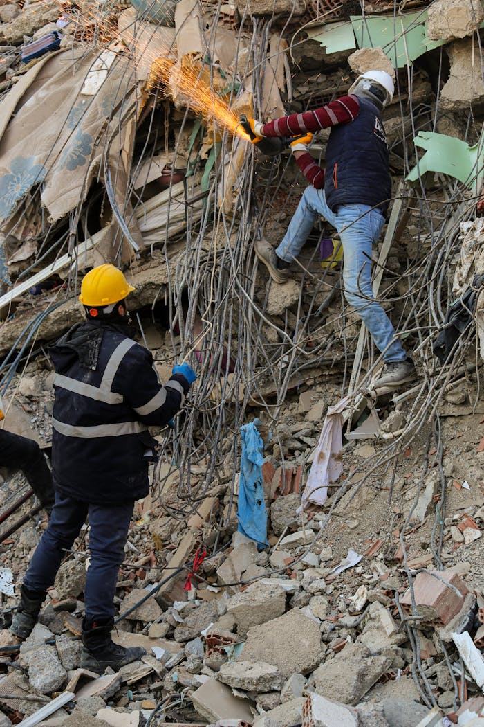 our-services-2 Rescue workers wearing helmets cut through rubble in a city disaster scene, working on recovery efforts.